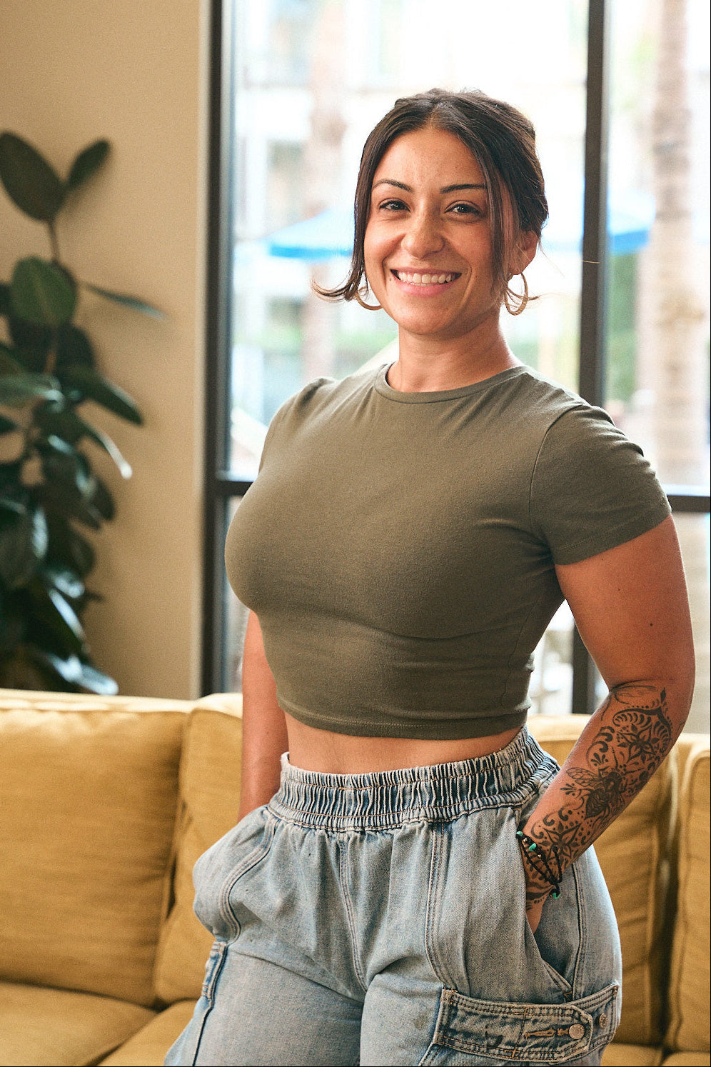 Woman standing in a living room wearing a green crop top and light blue jeans.